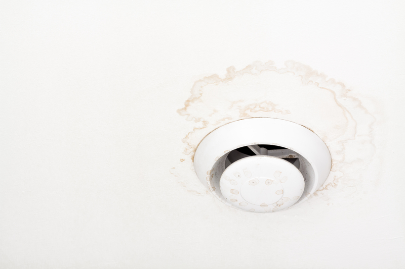 Round air ventilation frame on white ceiling with wet stains, streaks and mould around ventilator.