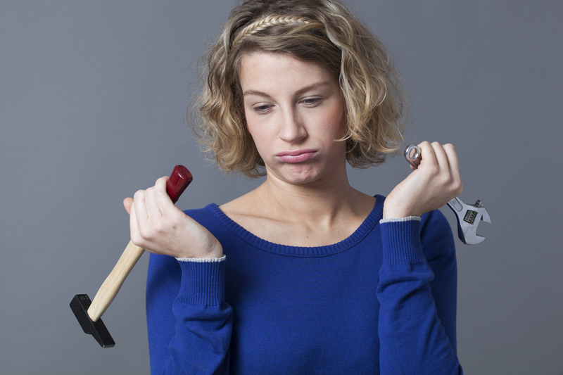 frustrated woman holding hammer and wrench while doing DIY project in home