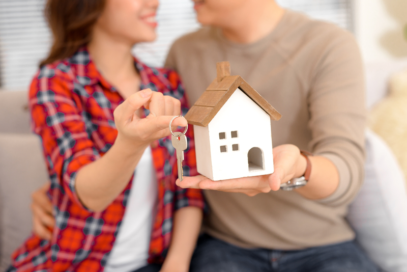 Happy couple holding keys to new home and house miniature - real estate concept